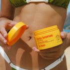 Person holding a jar of 'beta bronze' sunless tanning product with a green bikini.