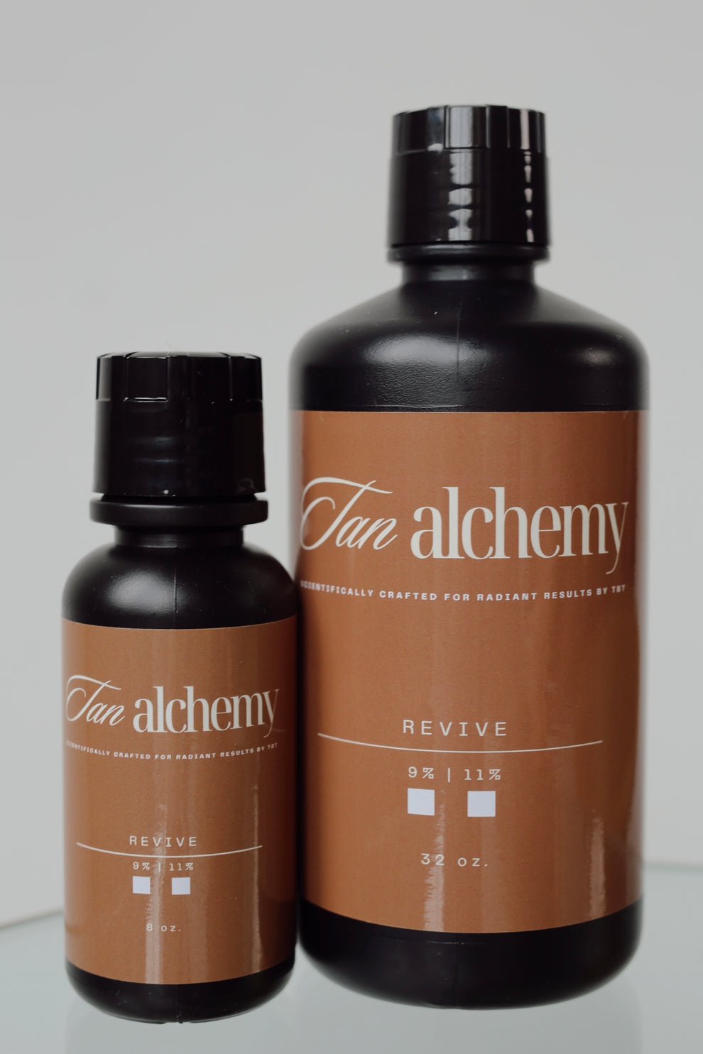 Two bottles of Tan Alchemy on a gray background