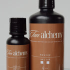 Two bottles of Tan Alchemy on a gray background