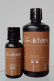 Two bottles of Tan Alchemy on a gray background