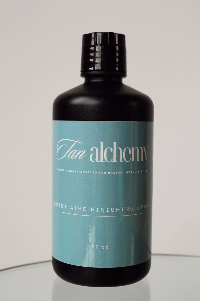 Bottle of 'Tan Alchemy' product on a reflective surface with a neutral background