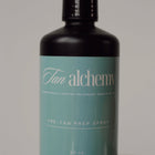 Black bottle with teal label featuring 'Tan alchemy' on a gray background