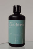 Black bottle with teal label featuring 'Tan alchemy' on a gray background