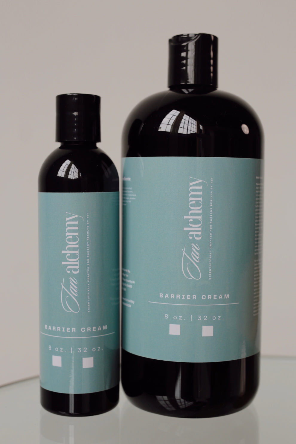 Two bottles of 'Two Alechemy' cream on a reflective surface with a neutral background