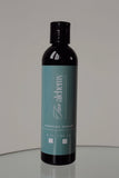 Bottle of 'The Alchemy' barrier cream on a reflective surface with a neutral background