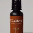 Brown bottle with black cap labeled 'Tan Alchemy' on a light gray background