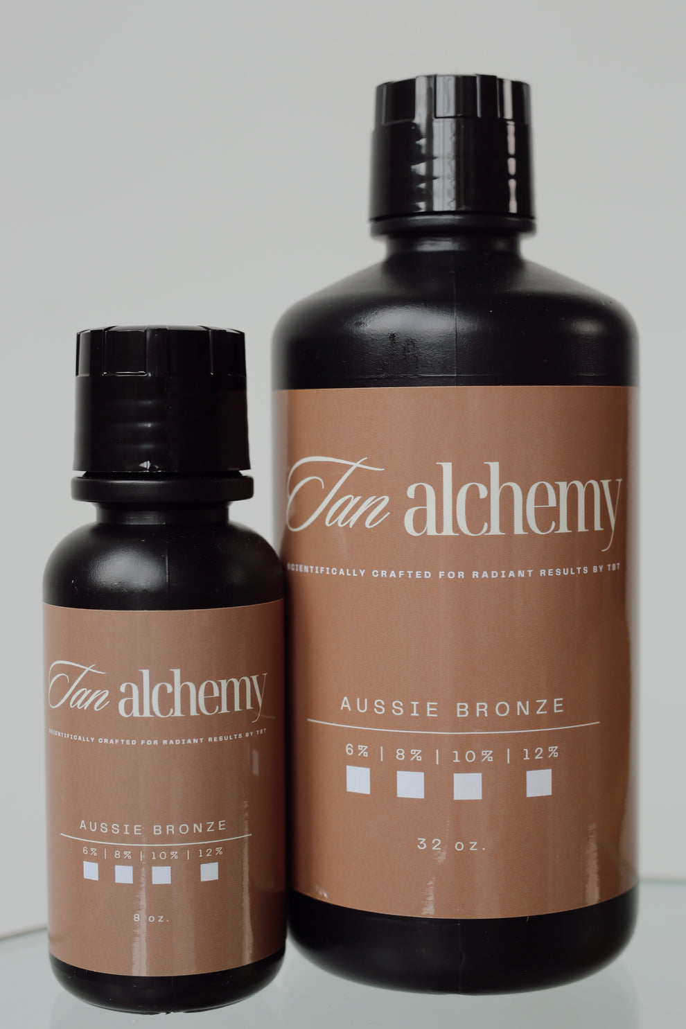 Two bottles of Tan alchemy Aussie Bronze tanning lotion on a light gray background