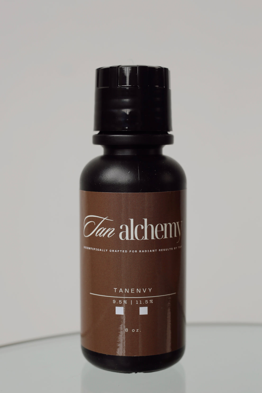 Brown bottle labeled 'Tan Alchemy' on a gray background