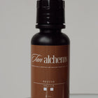 Bottle of 'Tan Alchemy Revive' on a reflective surface with a neutral background