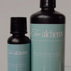 Two bottles of Tan Alchemy pre-tan prep spray on a gray background