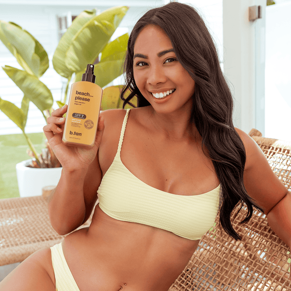 Woman in a yellow bikini holding a bottle of sunscreen with plants in the background