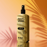 Gold bottle of b.tan 'beach... please' sunscreen spray on a warm gradient background