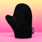 Black tanning mitt with 'b.tan' label on a pink and yellow gradient background