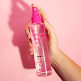 Hand holding a pink spray bottle labeled 'gimme the glow down' against a pink background