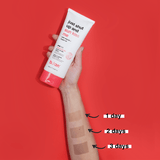 Hand holding a tube of sunscreen with application swatches on a red background