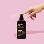 Hand holding a bottle of 'tanned AF' tanning product against a pink background