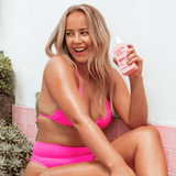 Woman in pink bikini holding a pink bottle tropic like it's hot in a bathroom setting