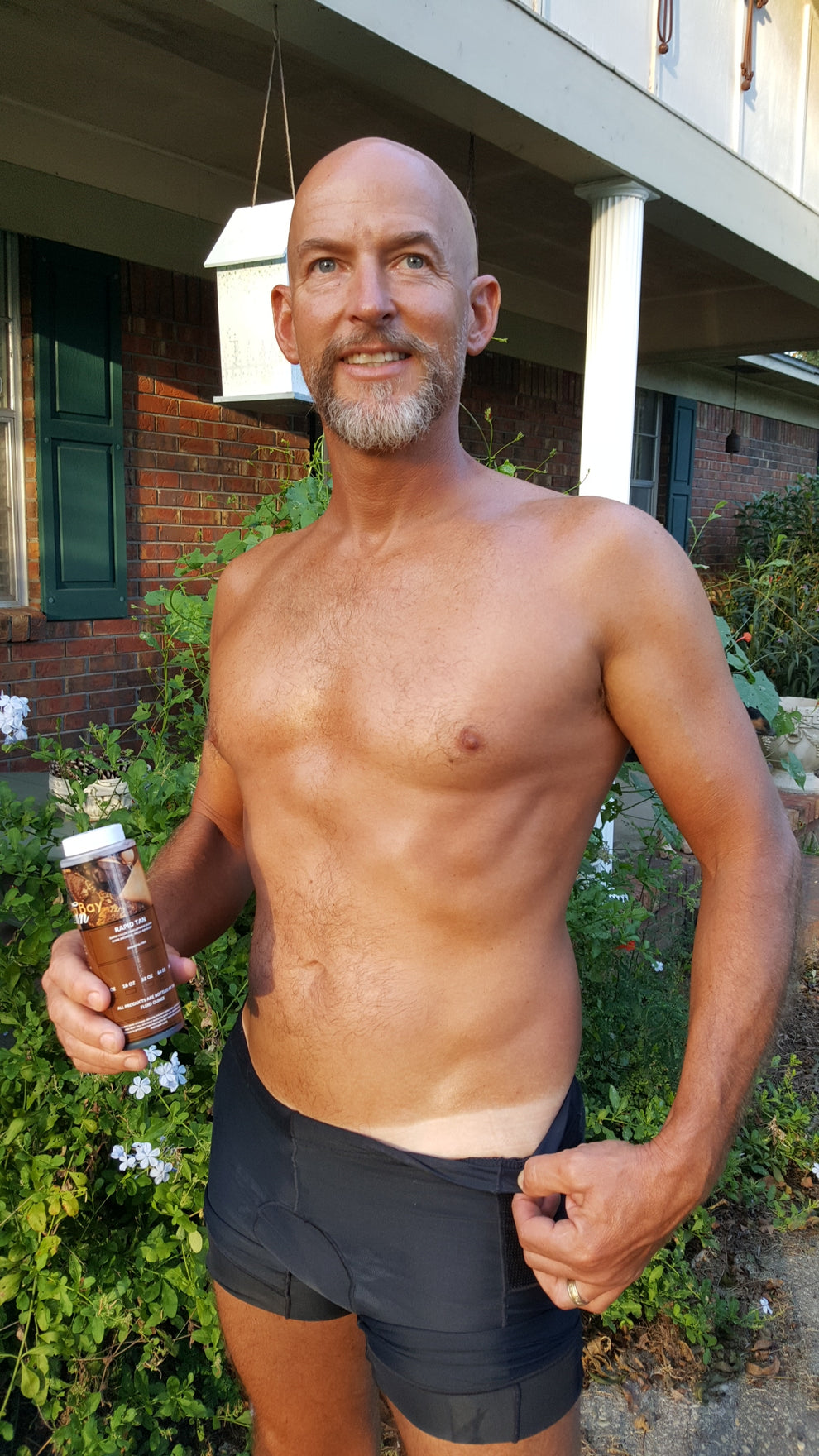Man outdoors holding Rapid Tan Spray Tan Solution , wearing black underwear